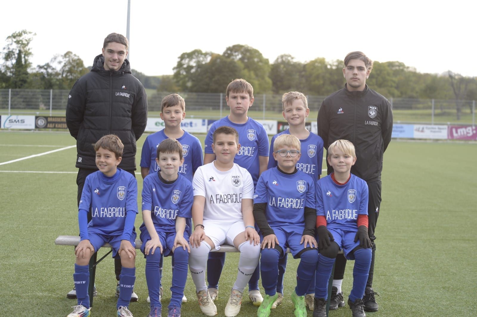 Youth soccer team posing on the field with two coaches, wearing blue and white uniforms.