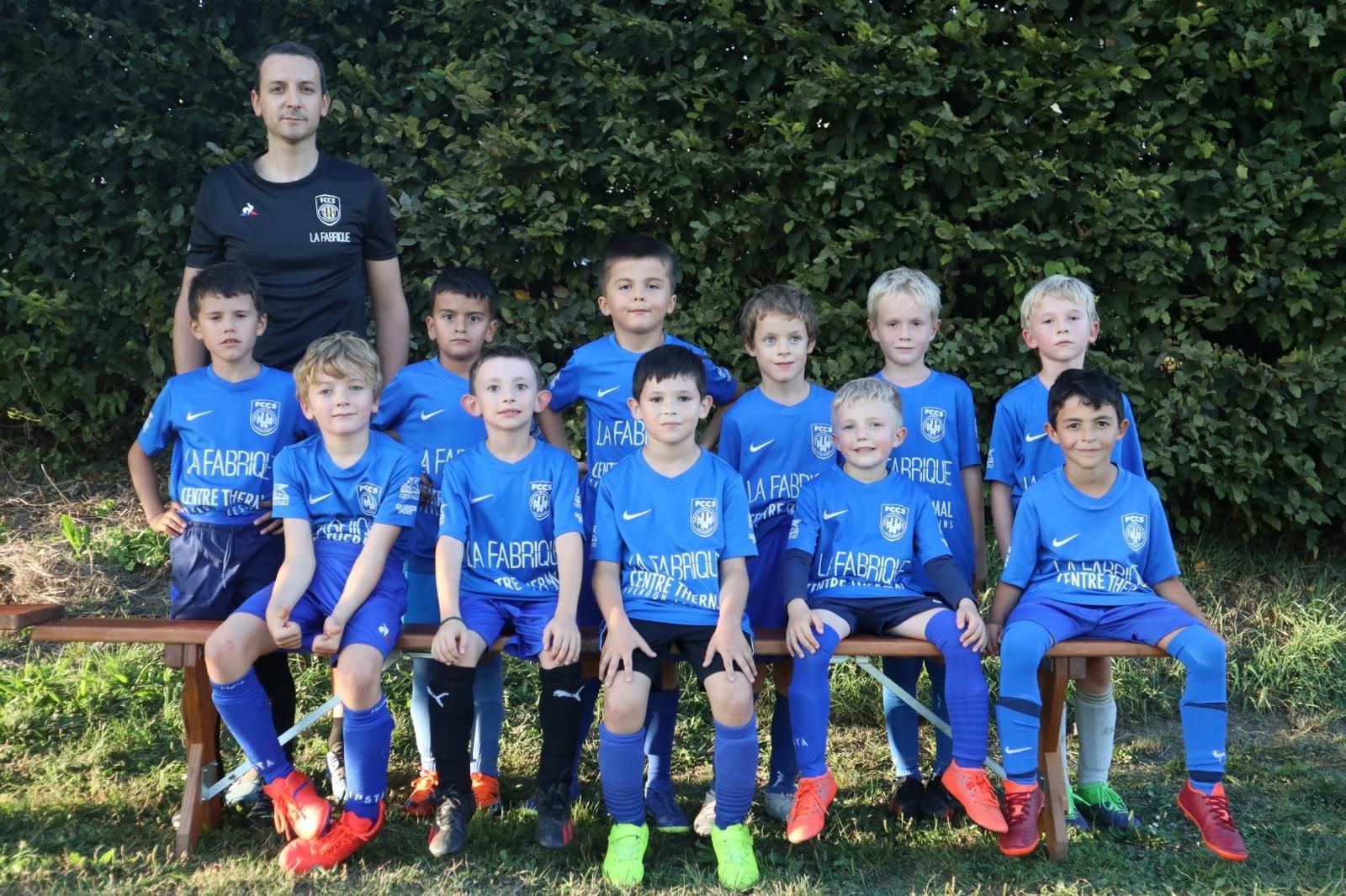 Group of young soccer players in blue uniforms posing for a team photo outdoors with their coach.
