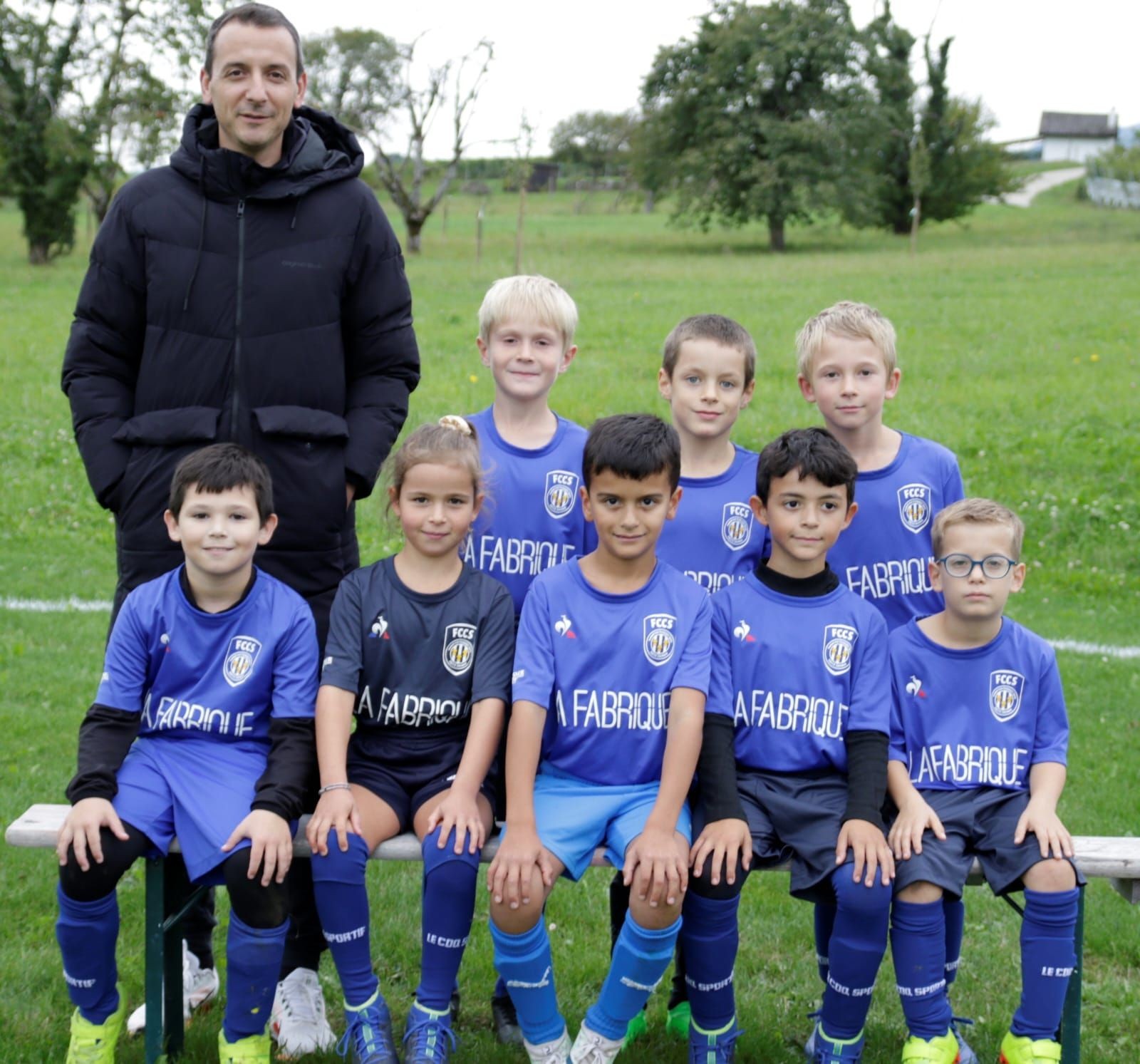 Group of young soccer players in blue uniforms, posing with their coach on a grassy field.