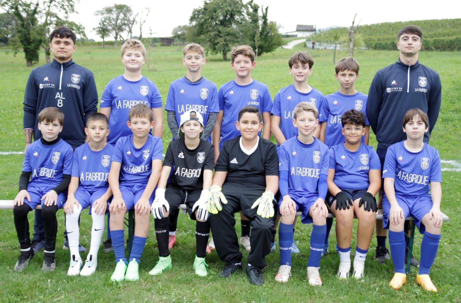 Youth soccer team in blue uniforms and coaches posing outdoors on a grassy field.