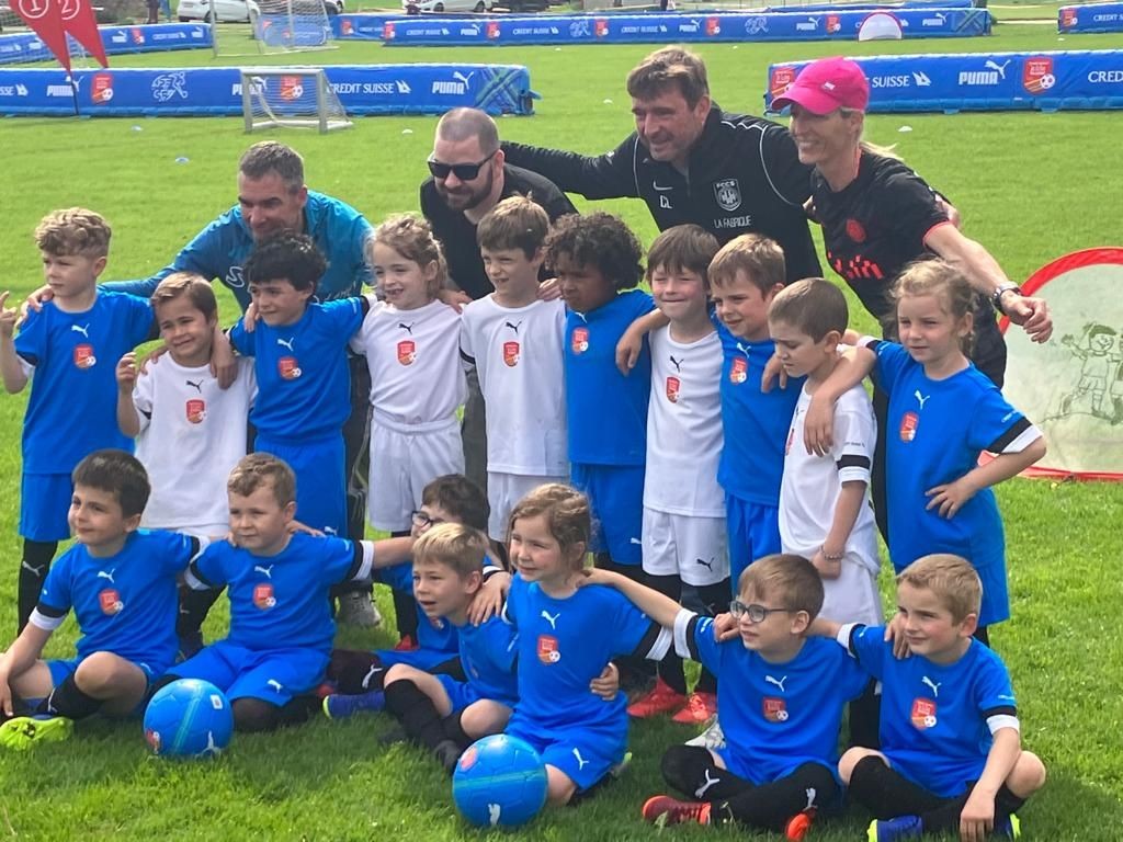 Young children in soccer uniforms posing for a group photo with their coaches on a grassy field.